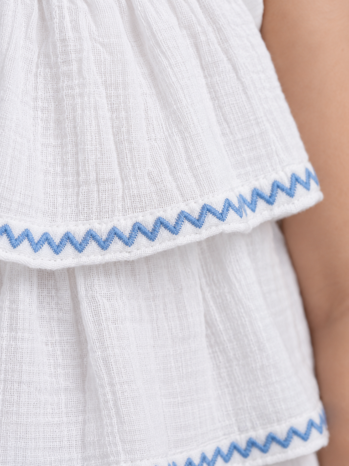 Close-up of light-blue zigzag embroidered edging and white double-gauze cotton muslin fabric